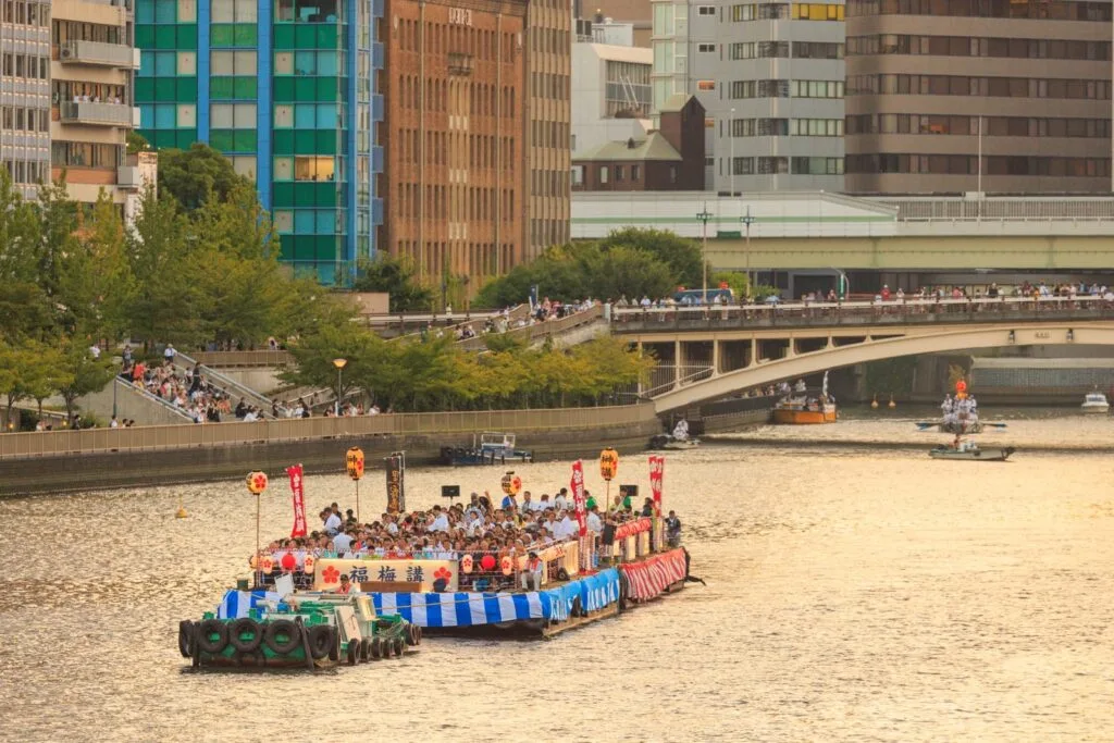 Tug boat pulls crowded barge down river at Tenjin Matsuri